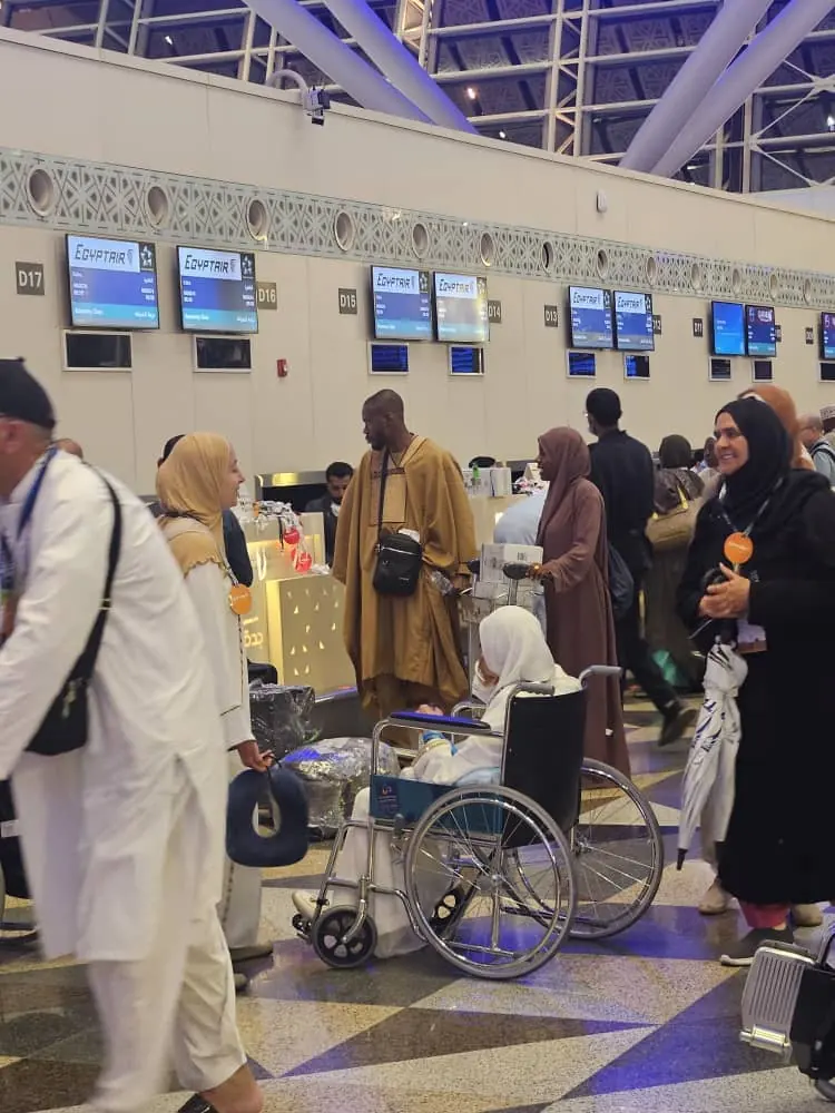 Pilgrims at airline check-in counters, including a traveller in a wheelchair